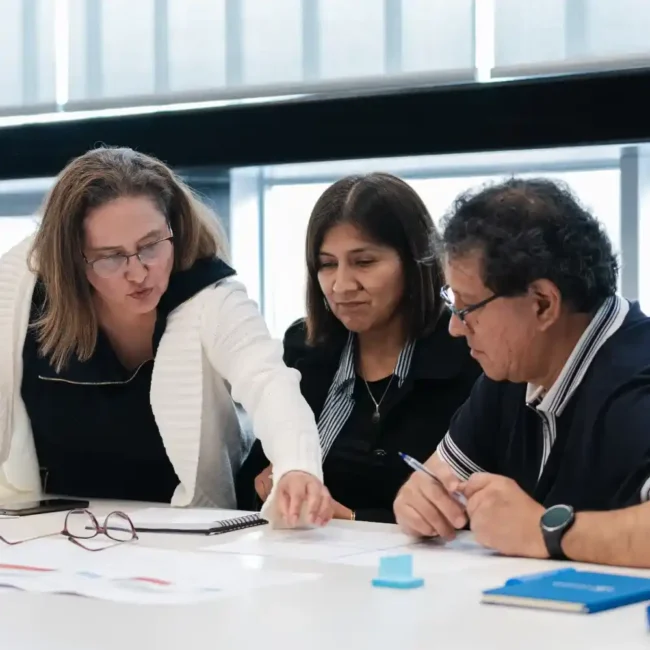 Tres colegas colaborando y revisando documentos juntos en una mesa