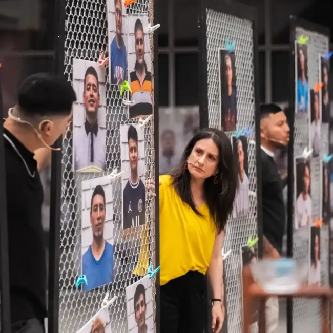 Mujer con camiseta amarilla observa un panel con fotografías de hombres sujetas con pinzas de colores